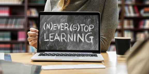 Notebook ist aufgeklappt und zeigt den Text "(N)ever (S)top Learning"