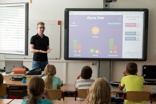 Ein Lehrer steh mit einem Smartboard vor einer Klasse Schüler*innen