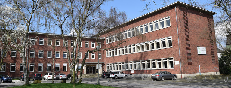 Gebäude der DAPF Bäume stehen vor einem Ziegelsteingebäude.