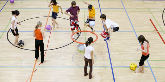 Kinder in einer Turnhalle, die mit übergroßen Schaumstoffwürfeln Übungen machen