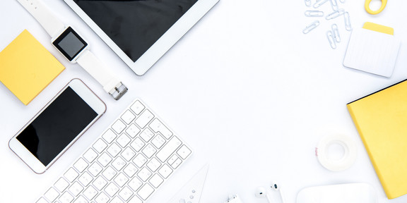 Organisation Utensilien In weiß und gelb gehaltene Gegenstände für die Organisation: Tablet. Büroklammern, Schere, Smartphone, Notizblock, Uhr, Tastatur, Post-It, Thesafilm, Lineal.