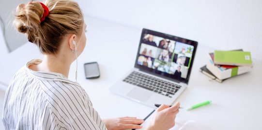 Am Schreibtisch sitzende Studentin tippt auf dem Laptop, daneben liegen Bücher und Stifte.