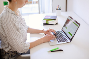 Am Schreibtisch sitzende Studentin tippt auf dem Laptop, daneben liegen Bücher und Stifte.