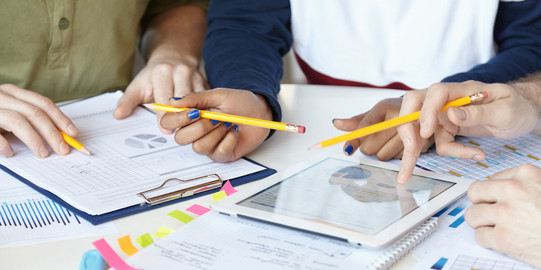 Diagramme_03 Auf einem Tisch liegen Blöcke und Blätter, ein Tablett, welches von einer Hand benutzt wird.